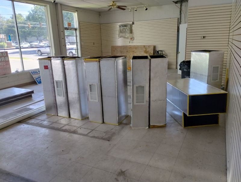 Sections of insulated sheet-metal ductwork staged inside an empty commercial storefront