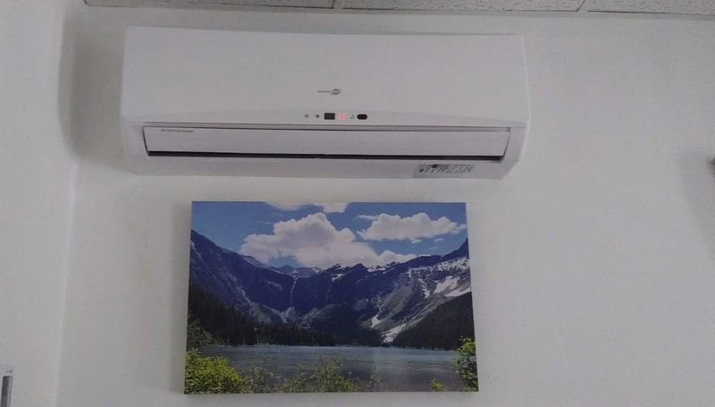 Ductless mini-split indoor unit mounted high on a wall above a framed landscape print