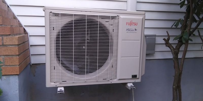 Fujitsu Halcyon mini-split outdoor unit mounted on a wall bracket against white siding