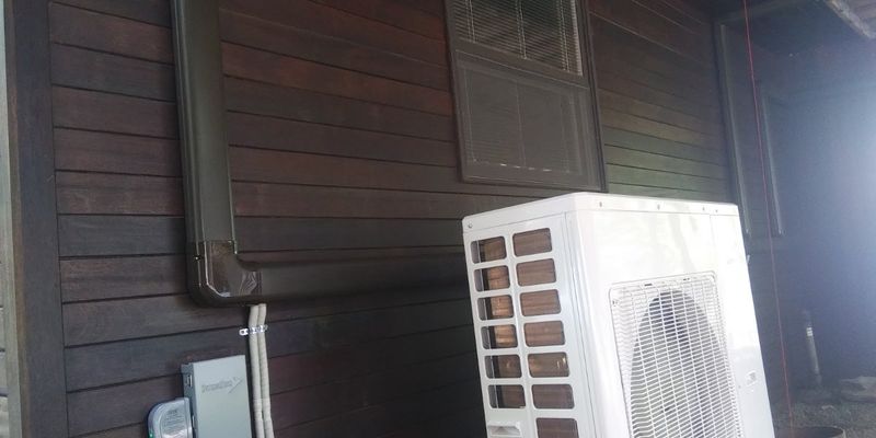Mini-split outdoor unit installed against dark wood siding with its own electrical disconnect
